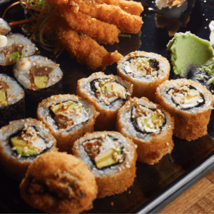 Un rollo de sushi con pollo teriyaki, queso crema y palta, tempura. El pollo teriyaki es marrón y brillante, el queso crema es blanco y cremoso, la palta es verde y cremosa, y la tempura es dorada y crujiente.