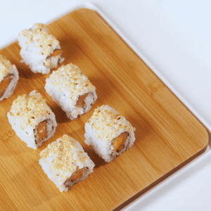 Un rollo de sushi con salmón, queso crema y palta. El salmón es rosado y brillante, el queso crema es blanco y cremoso, la palta es verde y cremosa.