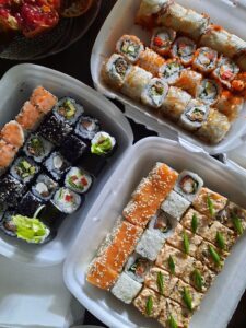 Una tabla de sushi de 60 piezas con una variedad de rollos, incluyendo California, tempura, panko frito, palta y hosomaki. Los rollos están envueltos en alga nori y rellenos de una variedad de ingredientes, como salmón, atún, kanikama, pollo, camarones, palta y queso crema.