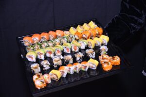 Una tabla de sushi de 50 piezas con una variedad de rollos, incluyendo california, tempura, sesamo, palta y hosomaki. Los rollos están envueltos en alga nori y rellenos de una variedad de ingredientes, como salmón, atún, kanikama, pollo, camarones, palta y queso crema